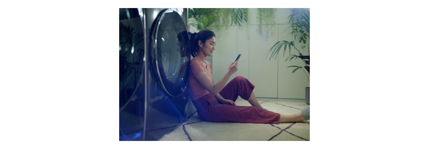 A woman using her phone while leaning against LG Washer 