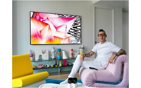 Karim Rashid sits next to the LG GALLERY DESIGN TV which is displaying his painting, DREAMSKAPE