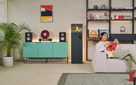 LG Styler ShoeCase is stacked up on top of the Styler ShoeCare in the living room while a man on the right is chilling on the couch.