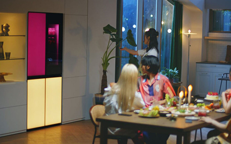 A woman is remotely playing music via a built-in Bluetooth speaker of the LG MoodUPTM refrigerator at the house party
