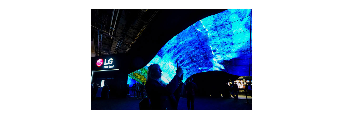 A woman taking a photo of the mesmerizing LG OLED Wave at CES 2020 as it displays vivid blue waves crashing against the coastline.