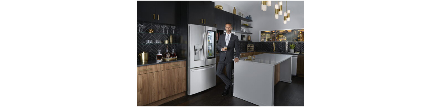 A man in suit standing in front of LG InstaView Door-in-Door™ refrigerator in a kitchen, holding a glass of beverage with Craft Ice™