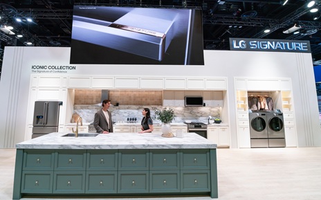 A man and a woman stand behind a green kitchen island in the LG SIGNATURE Iconic Collection display at LG’s booth during KBIS 2026, with a variety of LG SIGNATURE appliances in a kitchen setup behind them.