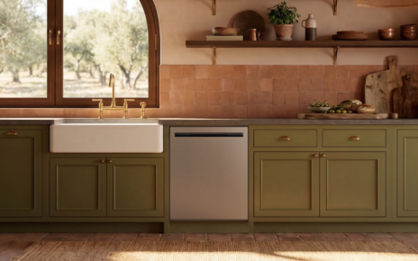 The new LG dishwasher is placed in a warm, rustic kitchen accented by olive-green cabinetry, natural wood textures and soft sunlight.