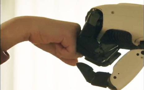 LG CLOiD gently fist-bumps a person’s hand against a softly lit indoor background.