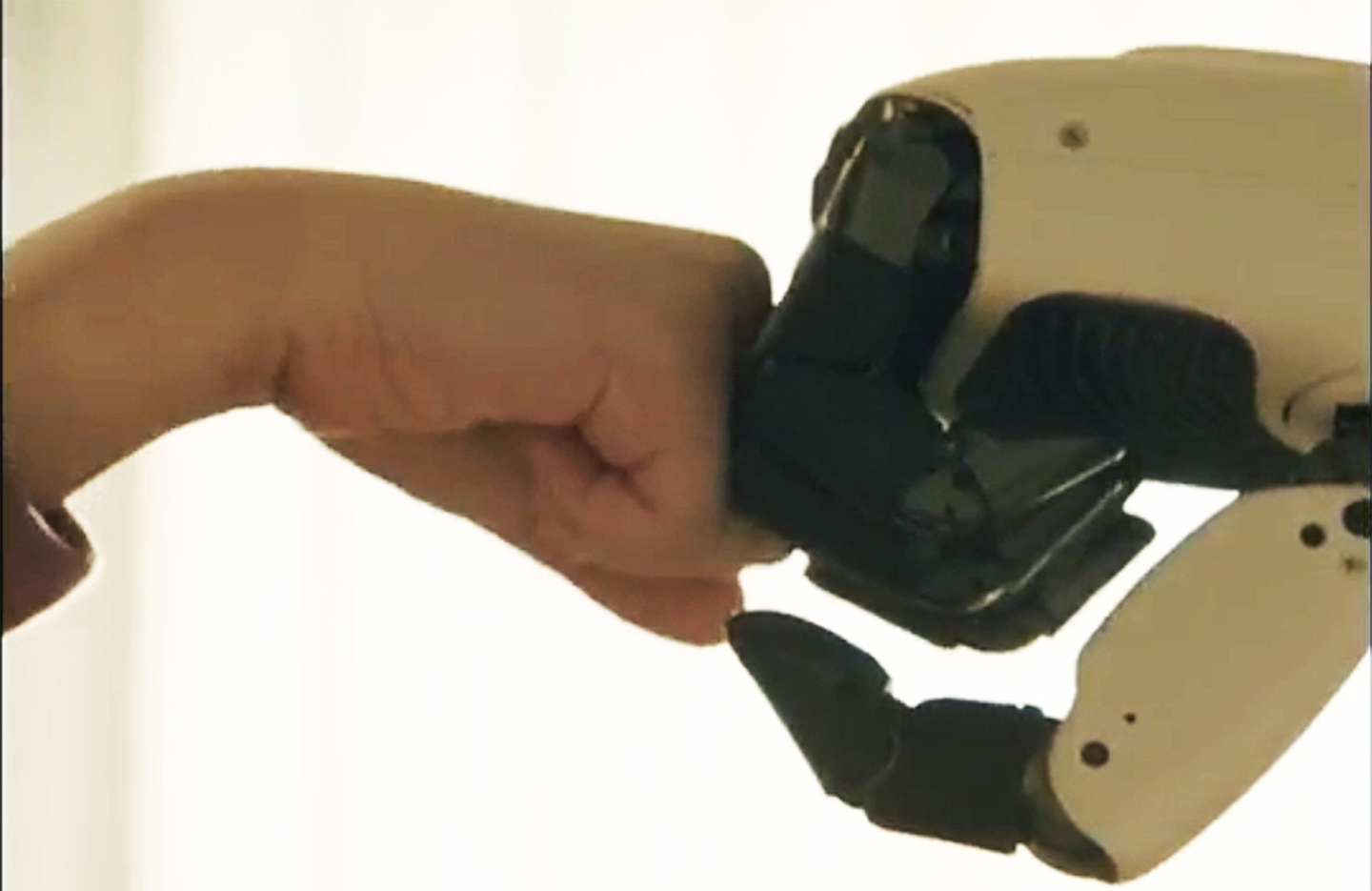 LG CLOiD gently fist-bumps a person’s hand against a softly lit indoor background.