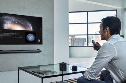 A man is watching LG TV supporting Amazon Alexa while holding the remote in one hand at home.