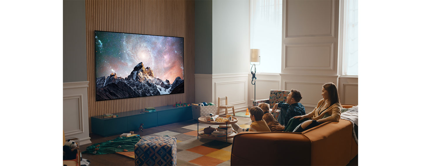 A family together in their living room enjoying spectacular natural landscape images on their wall-mounted 2022 LG OLED TV.