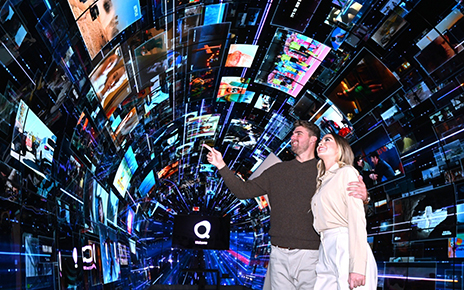 A man and a woman are pointing at the large variety of content playing throughout the LG webOS zone