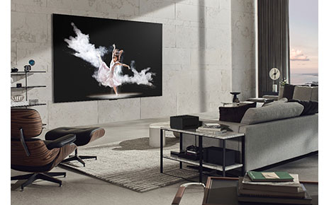 A wall-mounted LG SIGNATURE OLED M3 model displays an image of a woman performing ballet in a modern, gray-toned living room