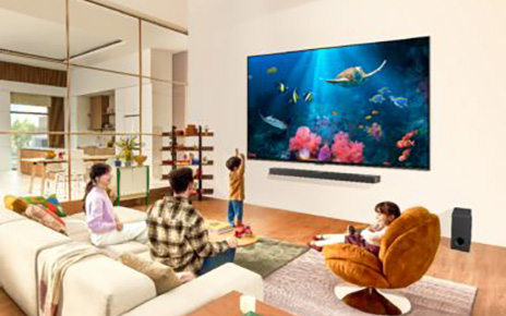 A family gathers around an ultra-large, wall-mounted LG QNED TV displaying an aquarium scene in their living room