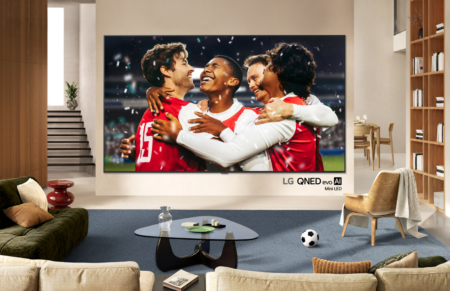 Four soccer players are celebrating a goal on the screen of a wall-mounted LG QNED evo Mini LED TV in a bright living room.