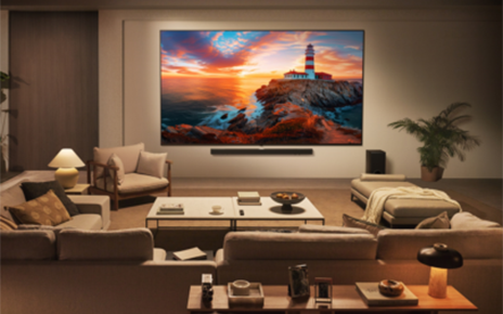 An LG QNED TV is mounted on the wall of a contemporary living room, displaying a coastal sunset landscape.