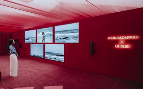 A woman stands in front of five wall-mounted LG OLED TVs, gazing at John Akomfrah’s artwork created in collaboration with LG OLED