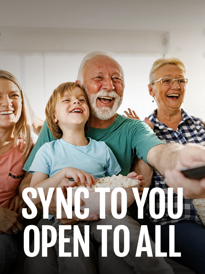 A family sits laughing while the grandfather points the remote outward. 	
