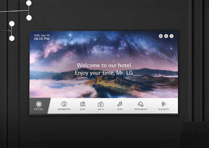 A wall in a dimly lit room features an LG TV, displaying a welcome message using the LG Pro:Centric Direct solution.