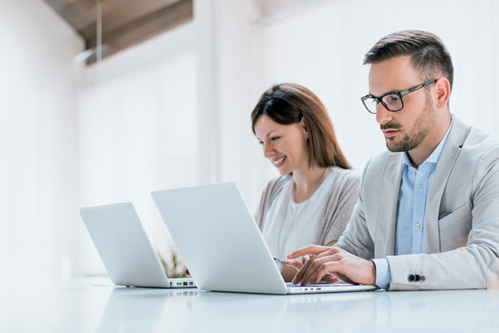 Two administrators are managing devices using LG SuperSign Control+ on personal PCs.