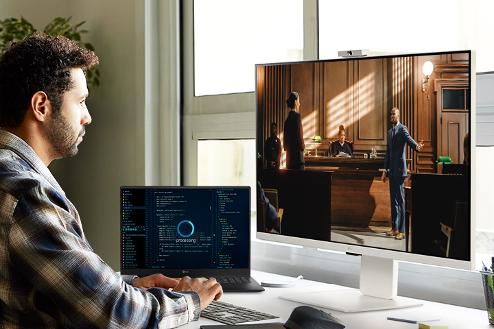 A man enjoying streaming content on the LG MyView Smart Monitor while waiting for laptop tasks to be completed.