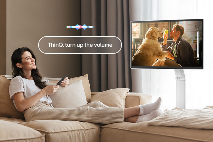 A woman is turning up the LG Smart Monitor Swing’s volume using a Magic Remote.