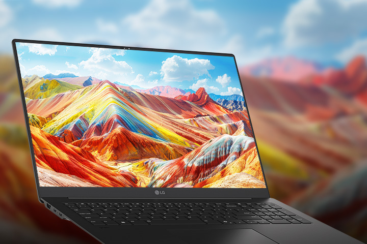 A laptop displaying a vivid and colorful landscape of vibrant mountains on its screen, emphasizing high-resolution and rich color reproduction. The background features a blurred version of the same landscape, drawing attention to the screen quality.