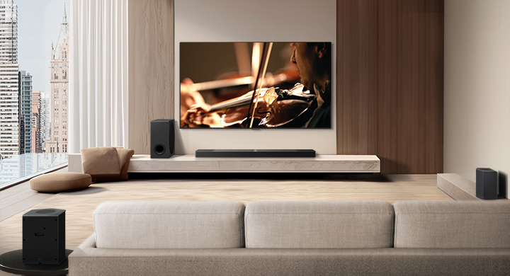 A video shows an LG TV, LG Soundbar, Rear Speakers, and Sub Woofer from behind the sofa in a modern city apartment. The Rear Speakers and Wireless Receiver light up, and a grid overlay appears over the image like a scan of the space. White beads of sound come together to make waves, then project from each part of the sound system, perfectly filling the room with sound. 