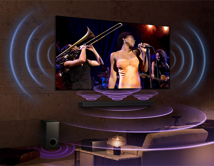 An image of an LG OLED TV in a room showing a music concert. Blue curved lines depicting TV sound and purple curved lines expressing Soundbar sound fill the space.