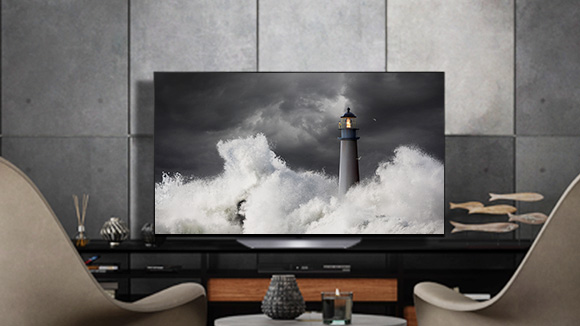 LG OLED B2 is in a gray room with stone walls, accessories, and chairs facing on to it