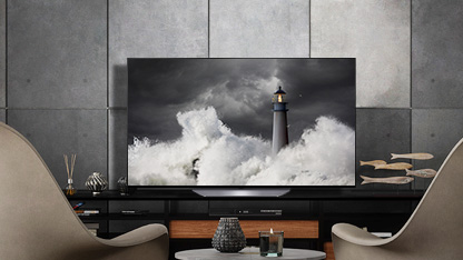 LG OLED B2 is in a gray room with stone walls, accessories, and chairs facing on to it