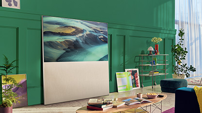 EASEL in Full View Mode leaning against a green living room wall and surrounded by art. There’s a scene of sand dunes on-screen.