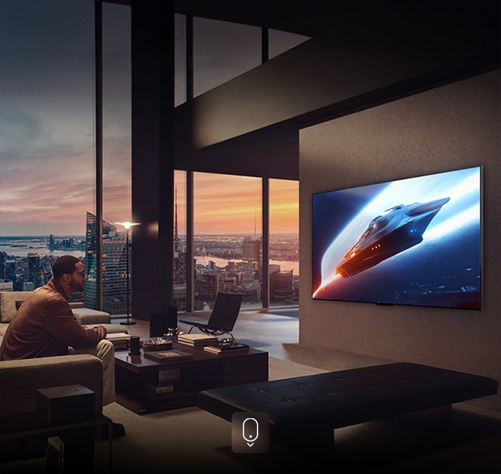 Classy living room in a penthouse apartment. Beautiful cityscape visible outside the window. A man is sitting on the couch watching content on the wall-mounted TV. 