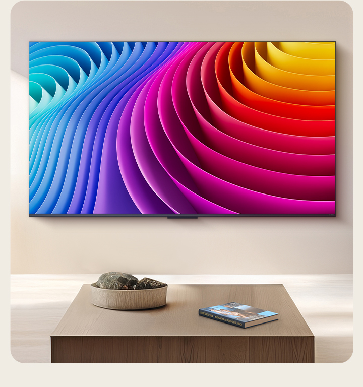 LG QNED TV is mounted on the wall of a beautiful, premium living room. On the TV is an abstract image that features a gradient of different hues that showcases how Dynamic QNED Colour Pro can render a wide range of Colours. 