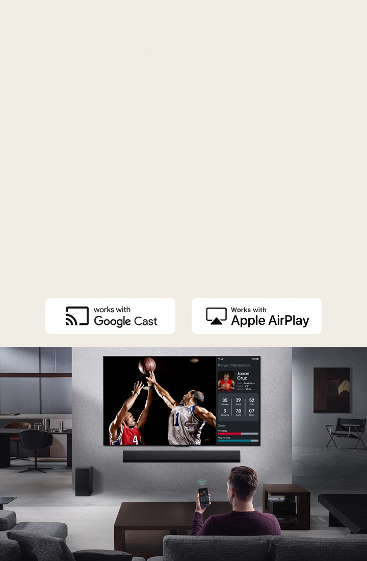Person in their living room holding their phone. On the phone is a transmitting icon showing that the phone screen is being mirrored on the TV. On the TV is a basketball game to the side is the mirrored screen, showing player statistics.