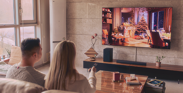Couple relaxing at home while watching a festive holiday scene on an LG TV during a cozy year-end evening.