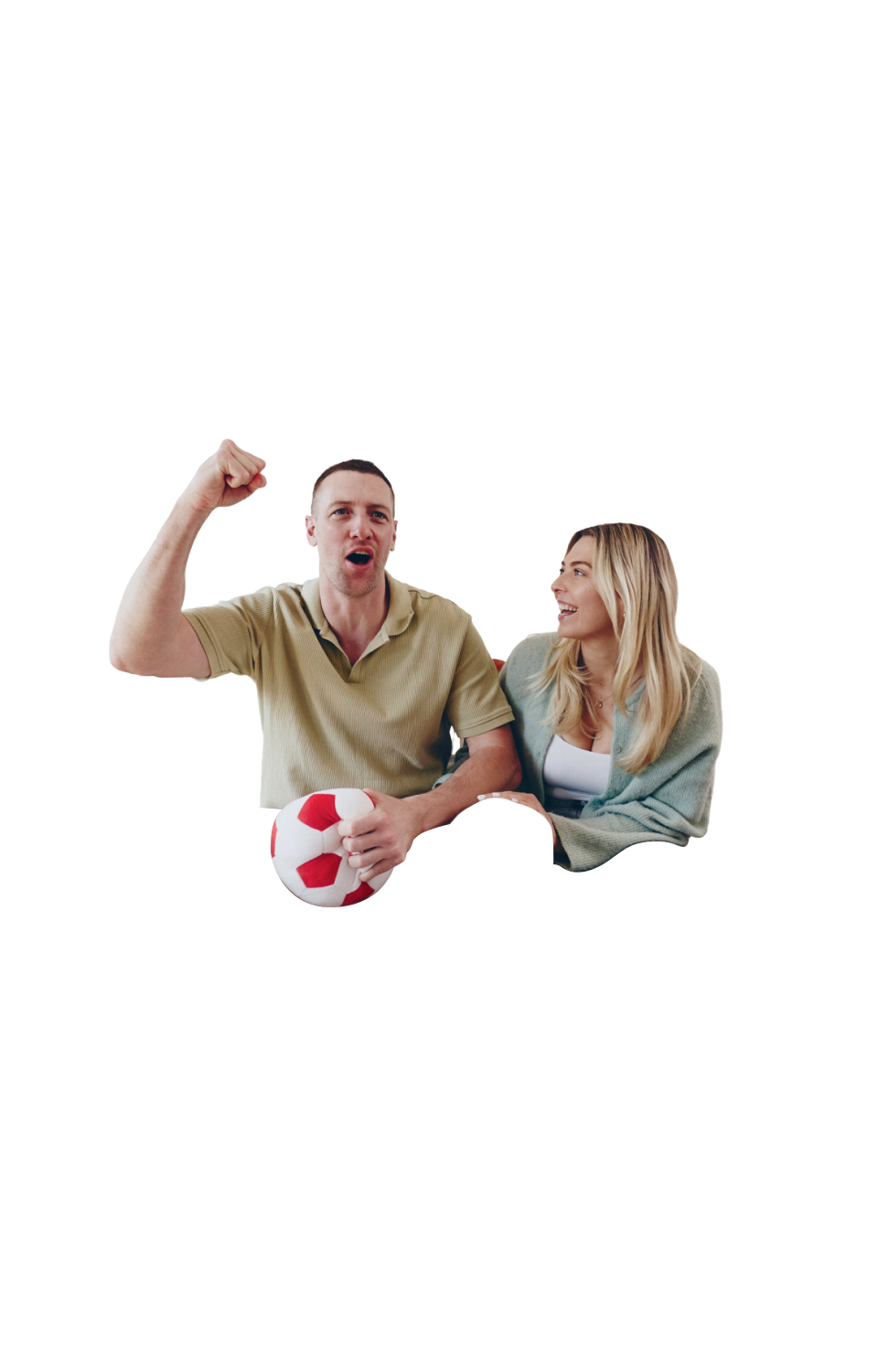 A man sitting on a sofa, cheering and holding a football plush toy, while a woman looks at him and laughs.