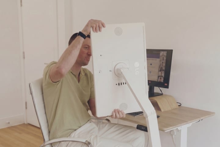 A man sitting on a chair and rotating an LG Smart Monitor Swing screen to a 90-degree angle.