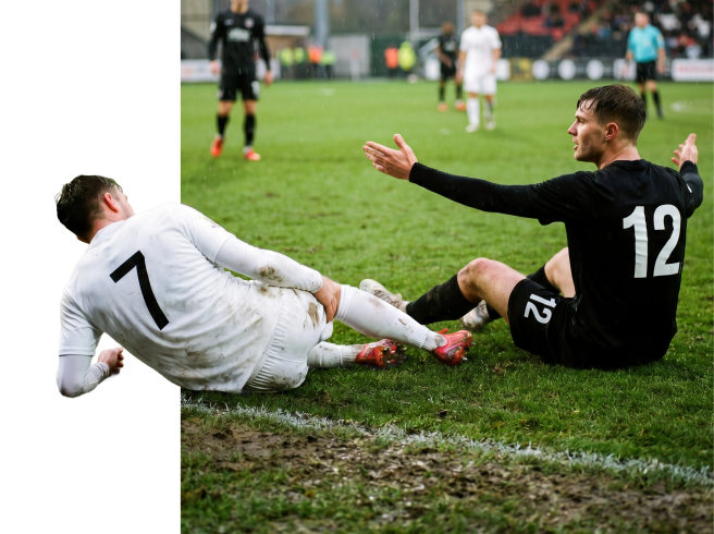 Two soccer players slide on a muddy field during a match, one in a white uniform and the other in a black uniform with the number 12, both reaching toward the ball.