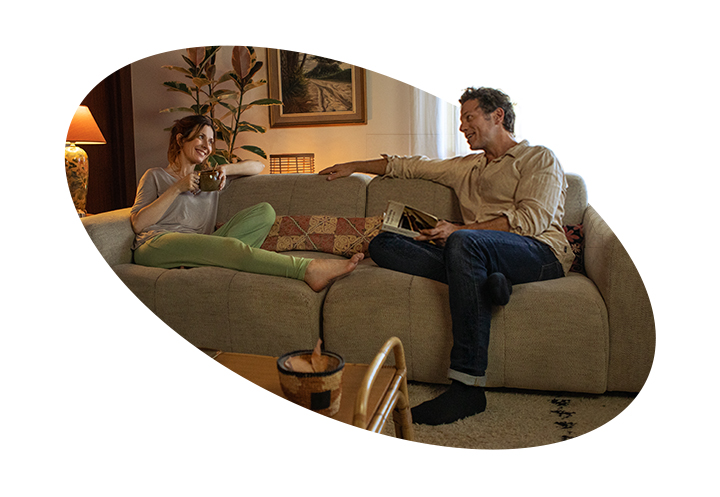 An adult woman and a man are sitting on a couch in the house and talking with a smile. There is a Quiet Mark certification logo next to the image.	