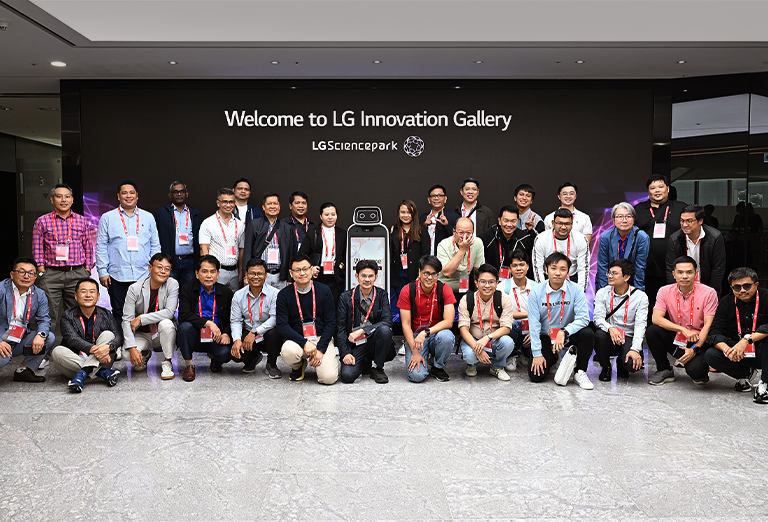 Group of people posing for a photo in front of the  'Welcome to LG Innovation Gallery' sign at LG Science Park.	