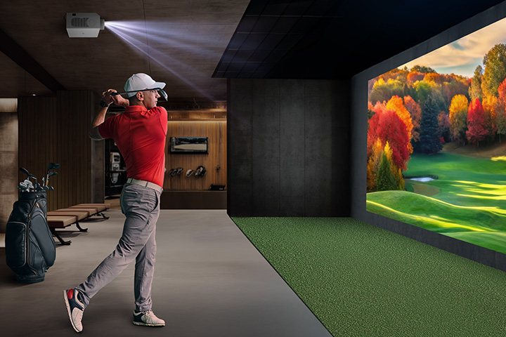 There is an indoor golf simulator with a golfer swinging and a vibrant autumn landscape projected on the wall.	