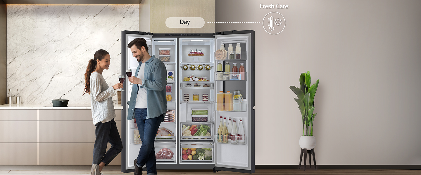 On the left side, The refrigerator is open and the couple is standing near the refrigerator.