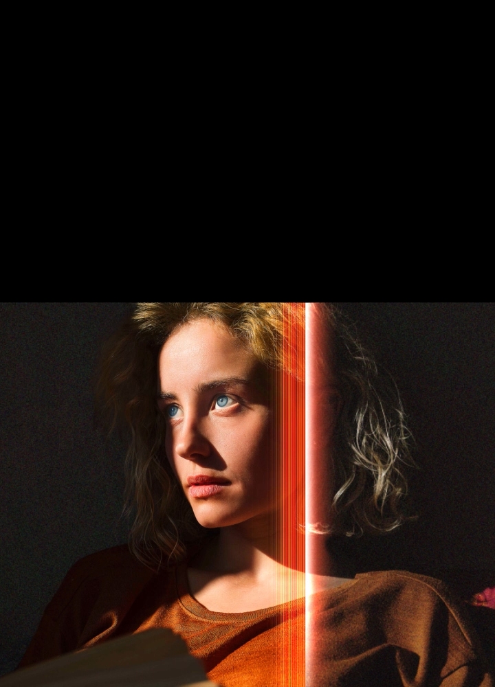 A woman with piercing blue eyes and a burnt orange top in a dark space. Red lines depicting AI refinements cover part of her face, which is bright and detailed, while the rest of the image looks dull.