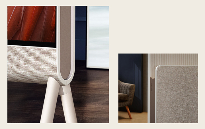 LG OLED Posé's bottom corner is seen closeup from the front focusing on the fabric, with wood flooring in the background.   The fabric of LG OLED Posé's Media Shelf and LG Objet logo are seen closeup with an armchair in the background.