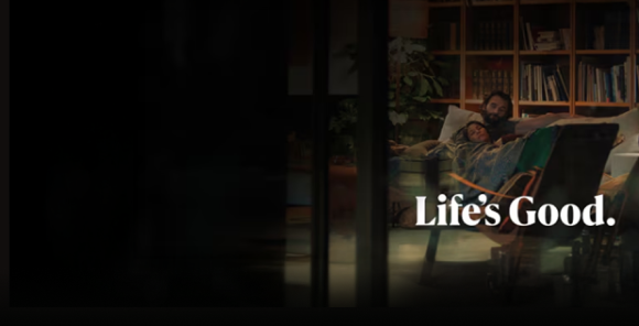 A man is sitting on a sofa in front of a bookshelf. A woman is leaning against the man's arm. The text Life's Good is written beneath the image.	