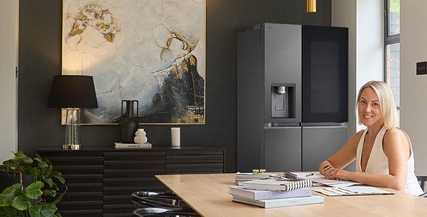 Woman working at a modern dining space with an LG refrigerator in a stylish, minimalist home interior.