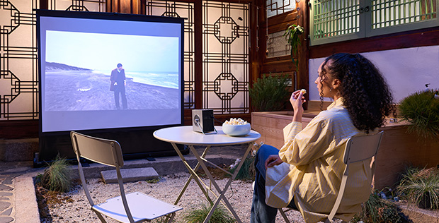 Woman enjoying an outdoor movie night in a traditional Korean hanok courtyard with a projector screen and snacks.