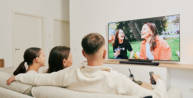 Family relaxing together on a sofa while watching happy moments on an LG TV during quality time at home.