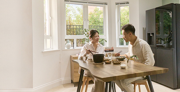 Couple enjoying a homemade meal together in a bright kitchen with an LG refrigerator and warm natural light.