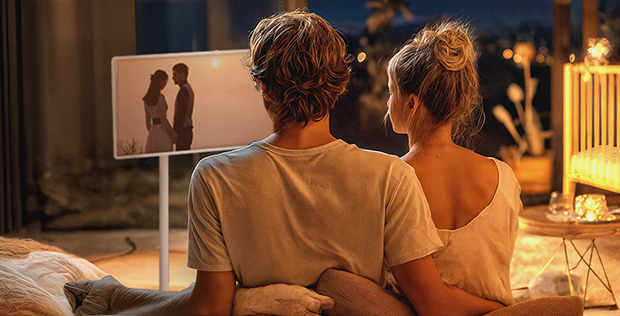 Couple relaxing together at home while watching romantic content on an LG StanbyME screen in a warm evening setting.