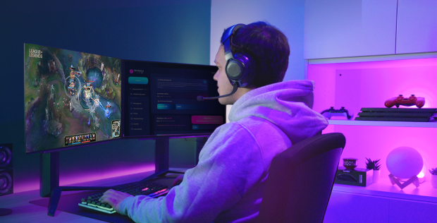 A gamer wearing a headset and playing on a dual-monitor setup with colorful LED lighting.