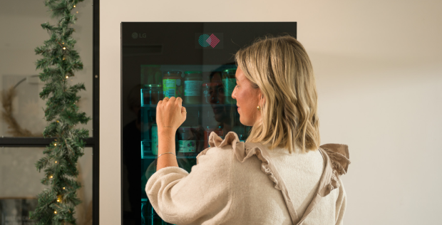 Woman enjoying a cosy Christmas at home with an LG refrigerator, surrounded by warm holiday decor and festive.